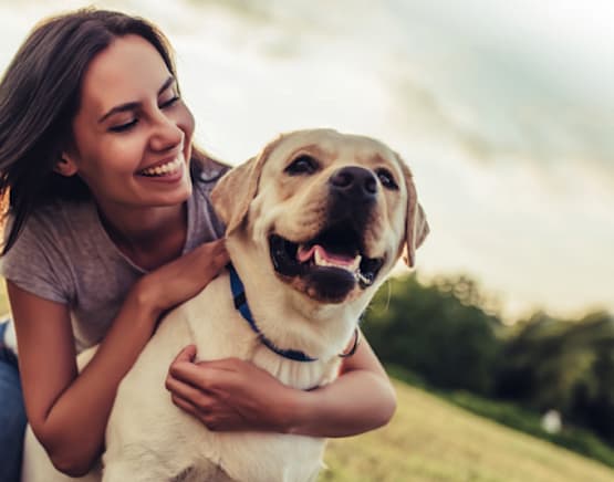Woman smiling and hugging a happy dog outdoors.