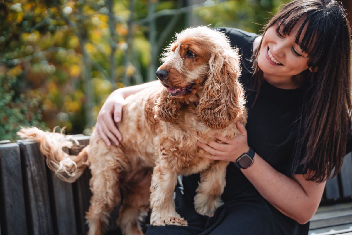 Woman smiling while holding a brown dog outdoors.