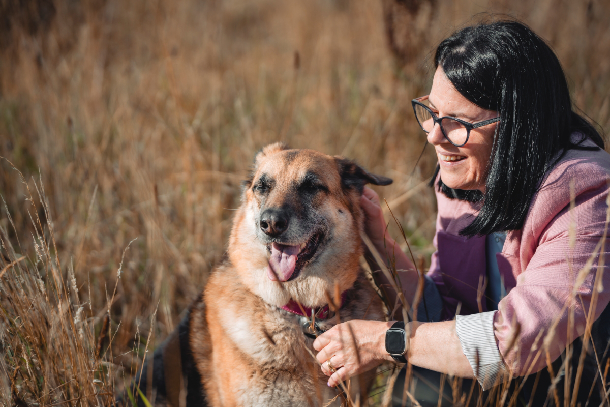 Woman smiling and petting a happy dog in a grassy field.