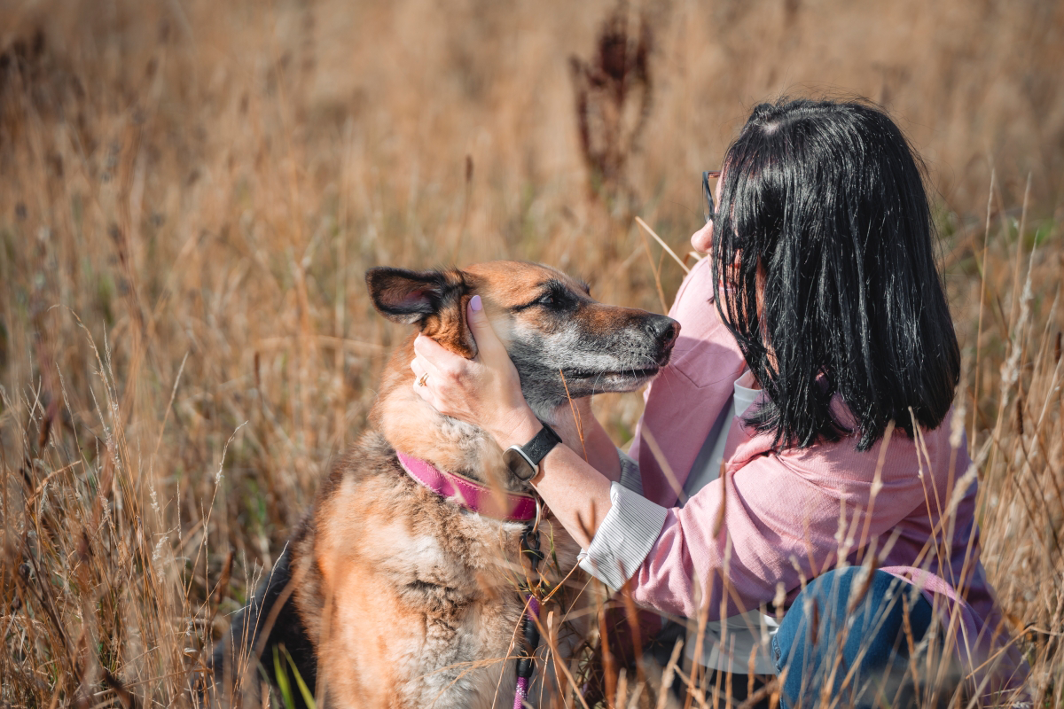 Woman in pink shirt hugging a brown dog in a field.
