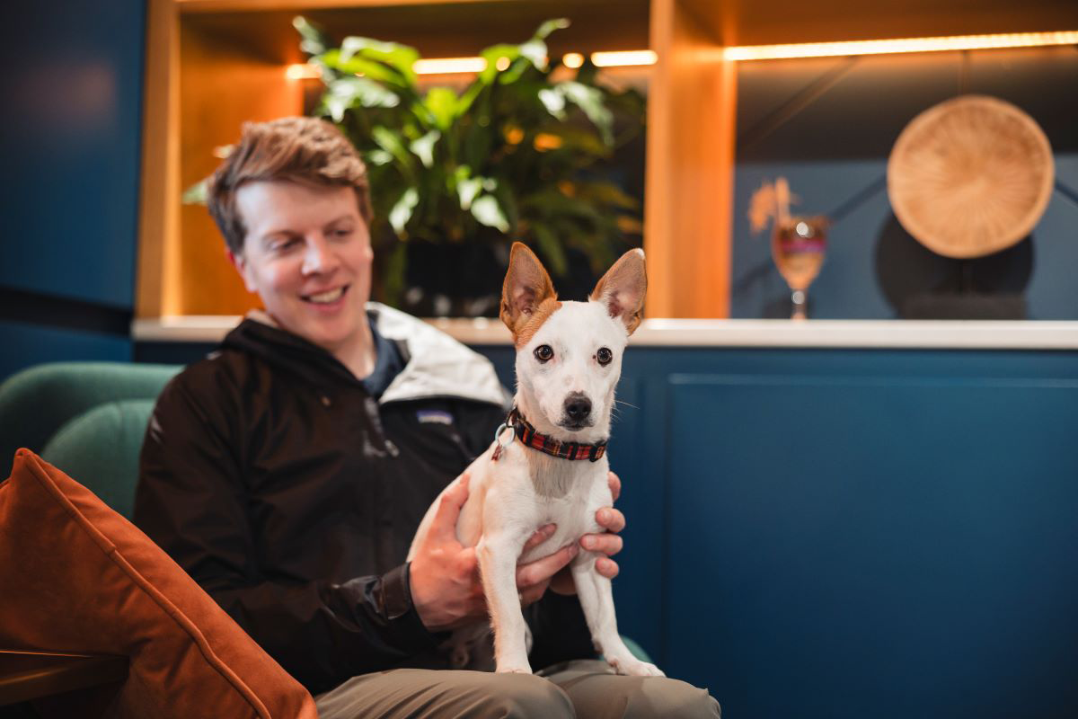 Person holding a small dog indoors with plants in the background.